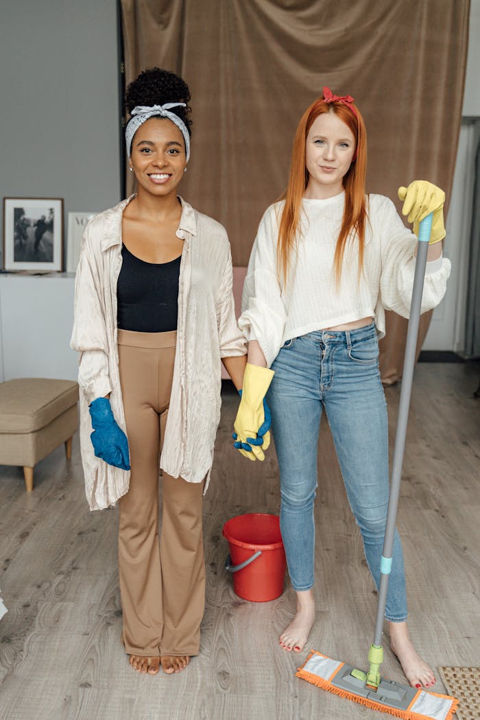 services-03 Two women smiling and holding hands while cleaning indoors, symbolizing teamwork.